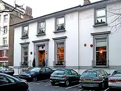 A two-storey white building with grey window frames, several cars parked in the foreground