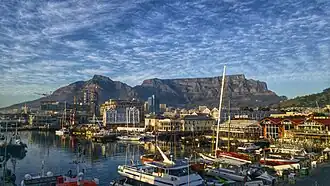 The V&A Waterfront, situated to the right of the port. Both are located in the City Bowl area, beneath Table Mountain​​‌