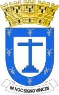 Silver leaves around the inside perimeter of a heraldic shield, in the center a blue cross and five golden towers atop