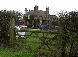 between two ragged hedges is a 5-bar gate, and over the gate can be seen the house that was once the railway station, a find brick and stone building with a Welsh slate roof and many chimmenys scatteed around the roofs.