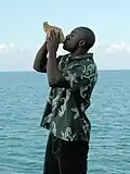 Man in olive Androsia blowing conch shell