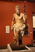 Colourful terracotta statue of a wizened, emaciated man, carrying a cross.