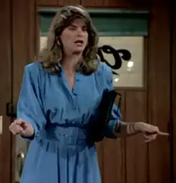 A brunette woman in a blue dress using both of her index fingers to point toward her view and wide away from each other.