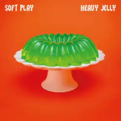A green jelly mould on a white platter on top of an orange surface.