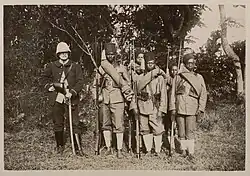 un officier en uniforme bleu foncé au côté de six tirailleurs malgaches en uniforme kaki