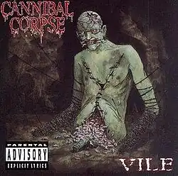 a green corpse with stitches on its chest, a mutilated head and face, and no lower body with maggots pouring from its innards. The corpse's penis appears to be lying in front of it.