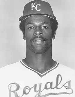 A man in a light baseball jersey and dark cap